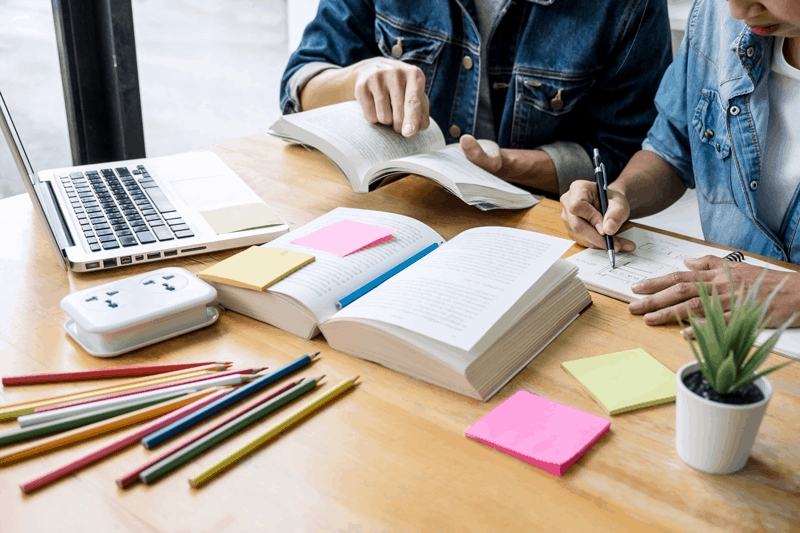 ersona estudiant amb llibres i ordinador per a preparació proves aptitudinals